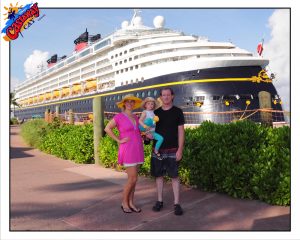 a couple holds a small child in front of huge disney cruise ship