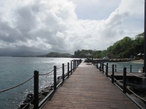a dock leading along the ocean towards a perfect sky with fluffy clouds and the green forest mountains of Grenada