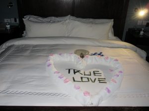 a hotel bed with a towl foleded into heart. the words true love in the middle in Grenada