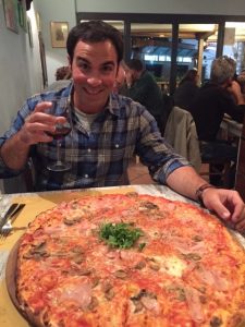 a happy man across a huge pizza in Italy