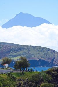 a distant mountain with puffy white clouds at the base a hill and the sea on the Azores Island Portugal