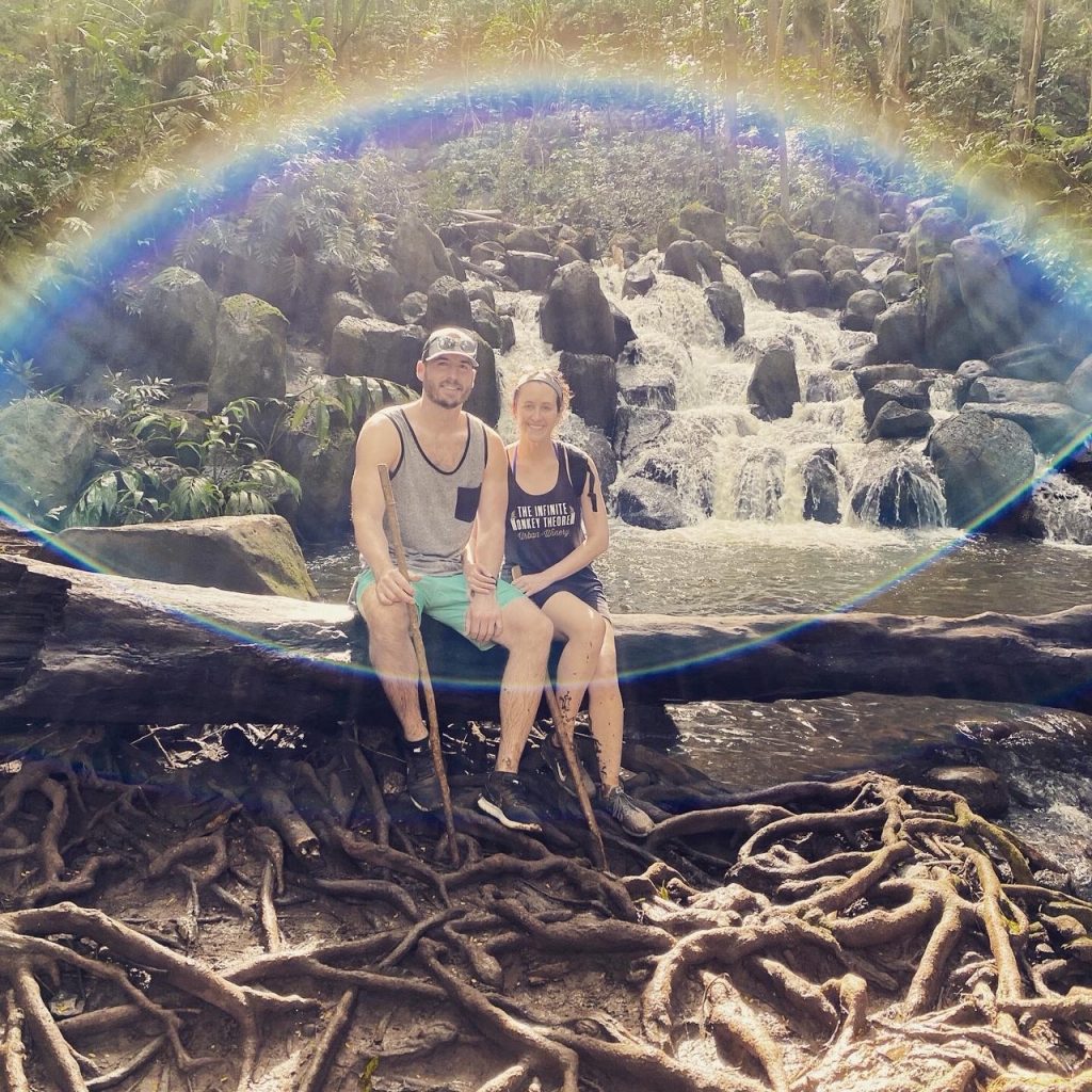 honeymoon couple sitting on a log in a rainbow in hawaii