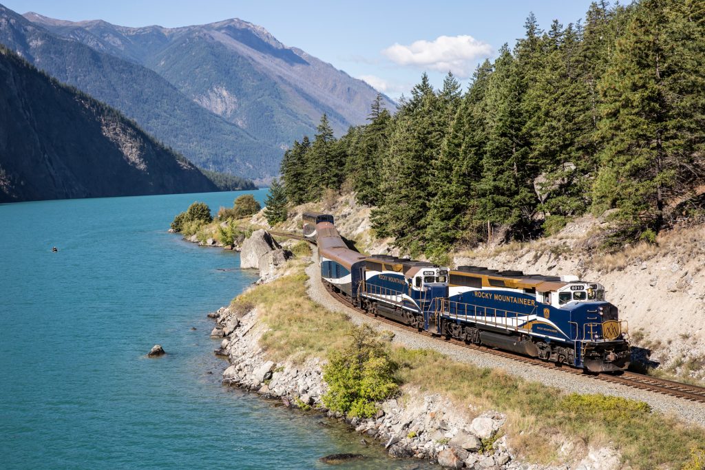 the Rocky Mountaineer train winding its way next to a blue lake in the Canadian Rockies