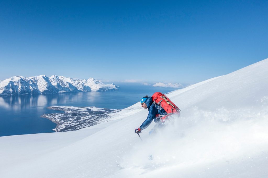 a man skiing down the slopes with the sea and mountains in the backgroun in Norway