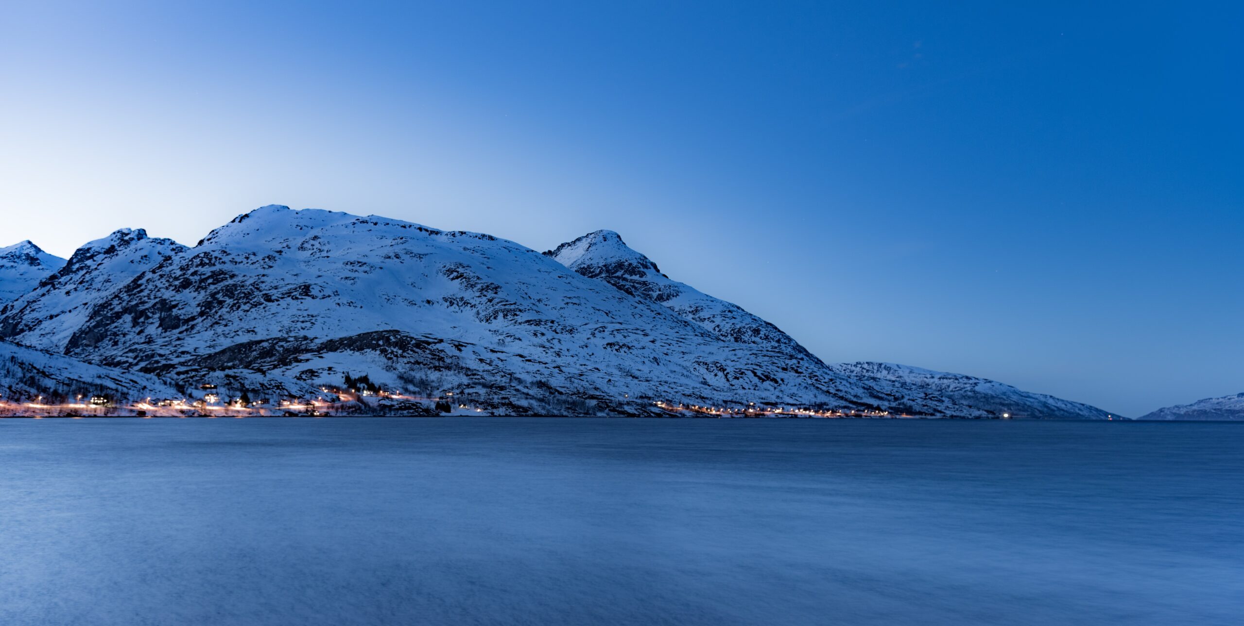 snow capped mountains and lights of a small village across the sea in Tromso Norway