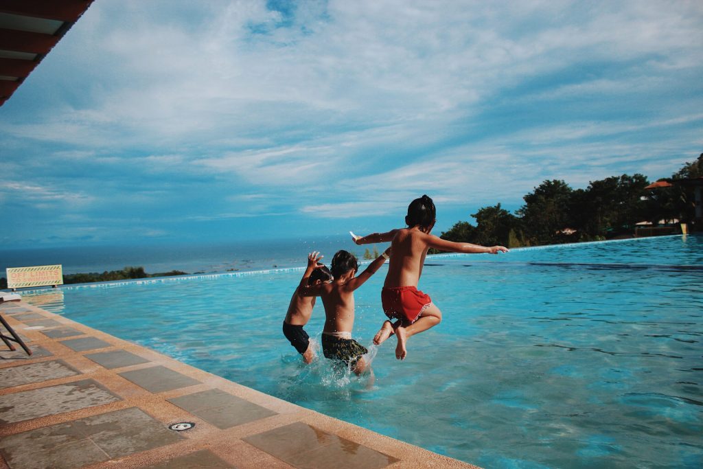 three young boys jumping into an infinity pool