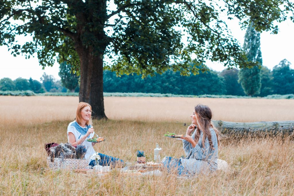 two women having a picnic in a field with a green tree
