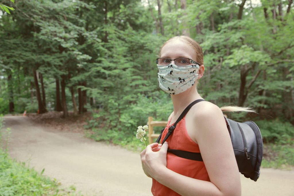 a woman wearing a mask with a small backpack on a forest trail