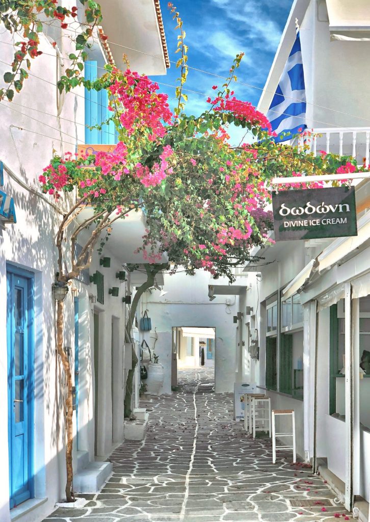 a small stone street with whitewashed buildings and bougainvilleas for boutique shopping in Greece