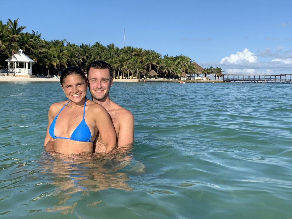 a cis couple in the ocean with an island of palm trees in the background at a resort in Mexico