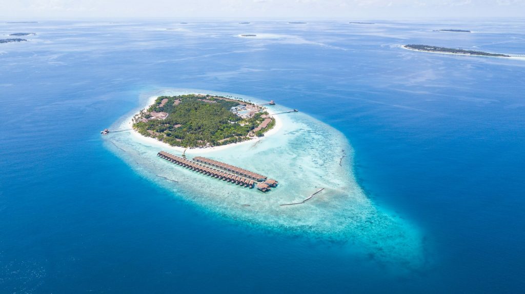 aerial shot of a private island with overwater bungalows in a deep blue sea in the Maldives
