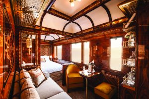 The interior of a sleeping car in the Venice Simplon Orient Express train - couch, seating are and bed with dark polished wood and gold trim