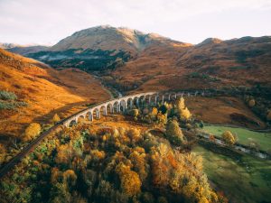 aerial view of the glennfinnan viaduct surounded by yellow and orange mountains in Scotland
