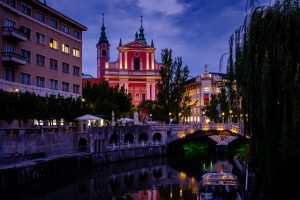 a church and other buildings lit up at night viewed from across the river in Slovenia