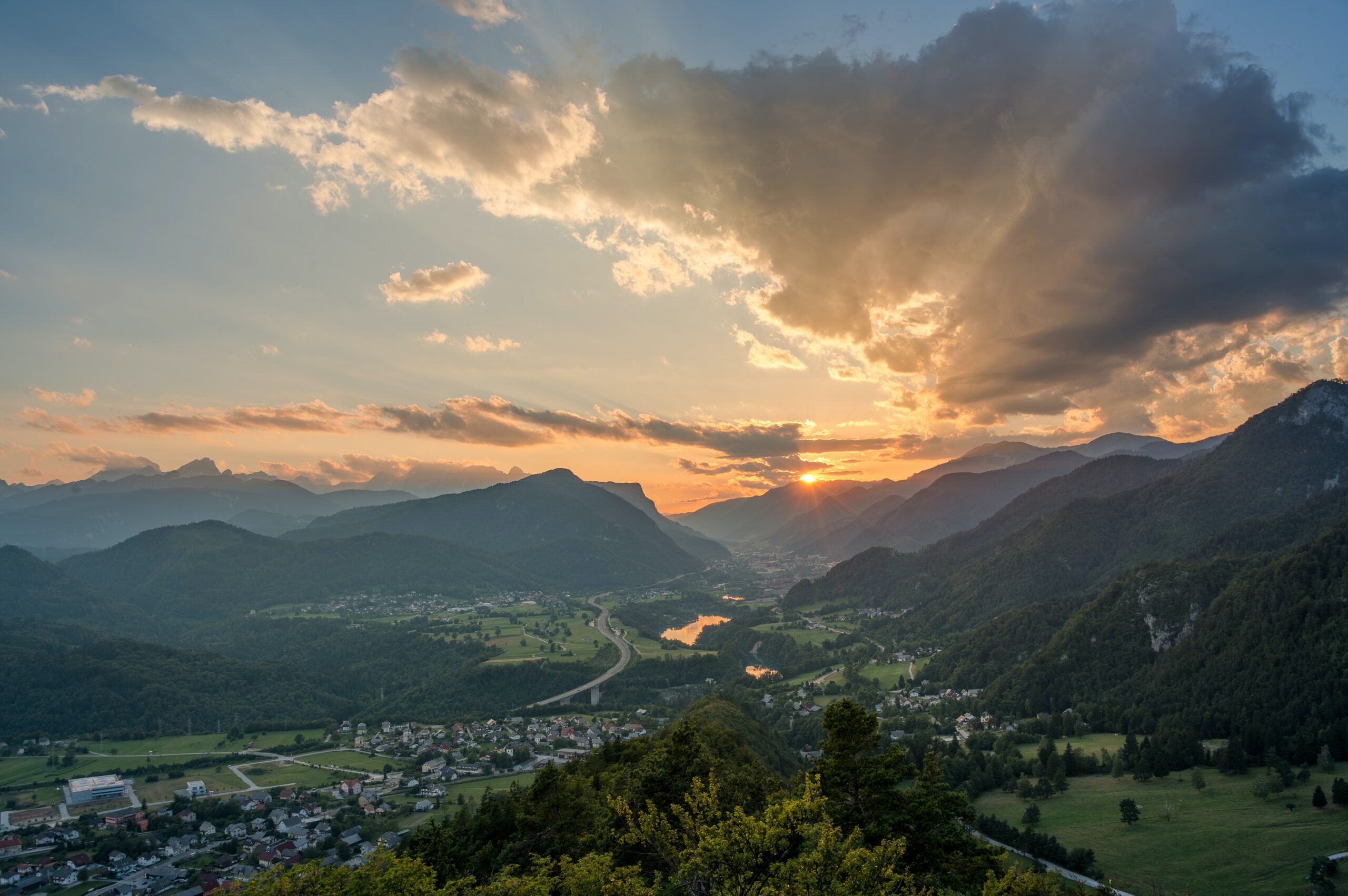 sunrise view looking down on a lush green valley with small lake and town in Slovenia