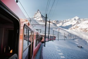 a red train traveling through snowy mountains towards the matterhorn in Switzerland