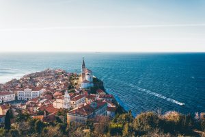 view of Piran Slovenia from a hill looking down on red roofs and a tall church spire that juts out into the sea