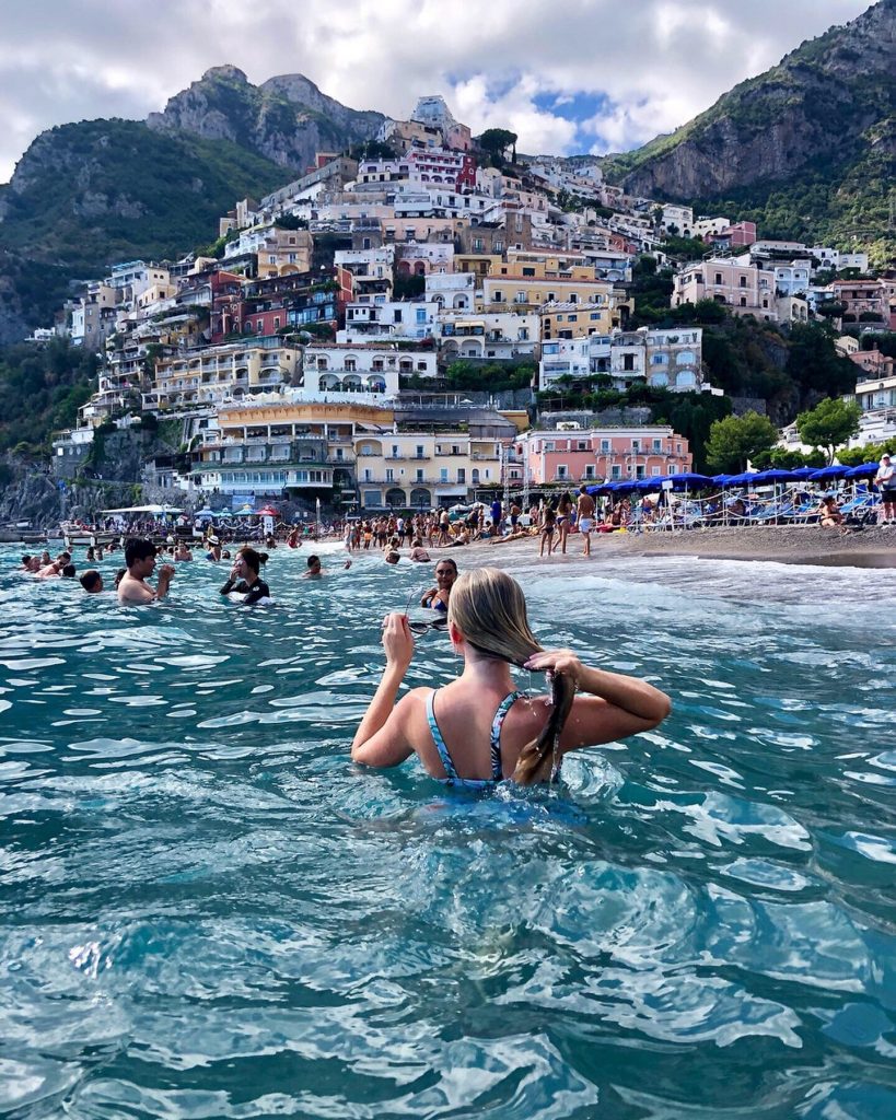 a woman in the sea looking at the colorful mountainous Italian city of Positano