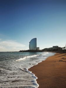golden sand and waves kissing the shore with the famous sail-shaped building in the background on Barcelonetta beach in Barcelona Spain