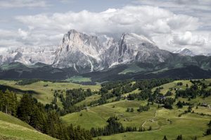 a green valley of hills with imposing craggy grey mountains in the background Dolomites Italy