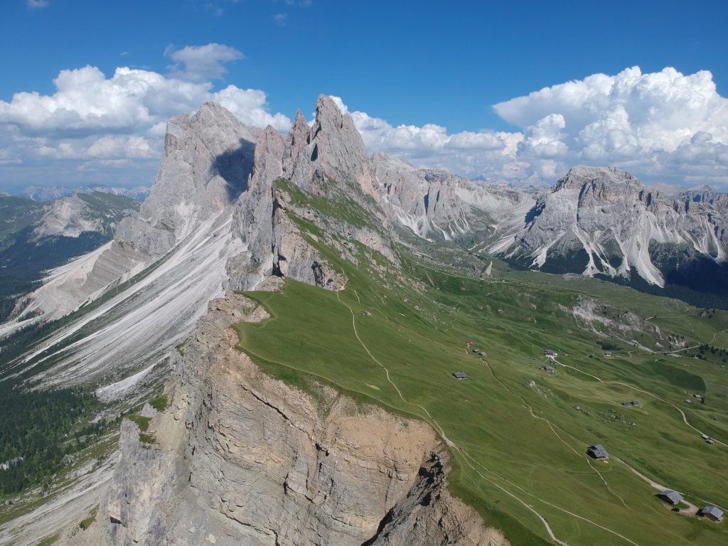 an imposing mountain ridge with a sheer drop on one side and soft grassy hills on the other and imposing mountains in the background Dolomites Italy