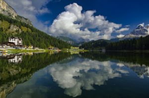 a large lake reflects the green trees and cloudy sky in the Dolomites
