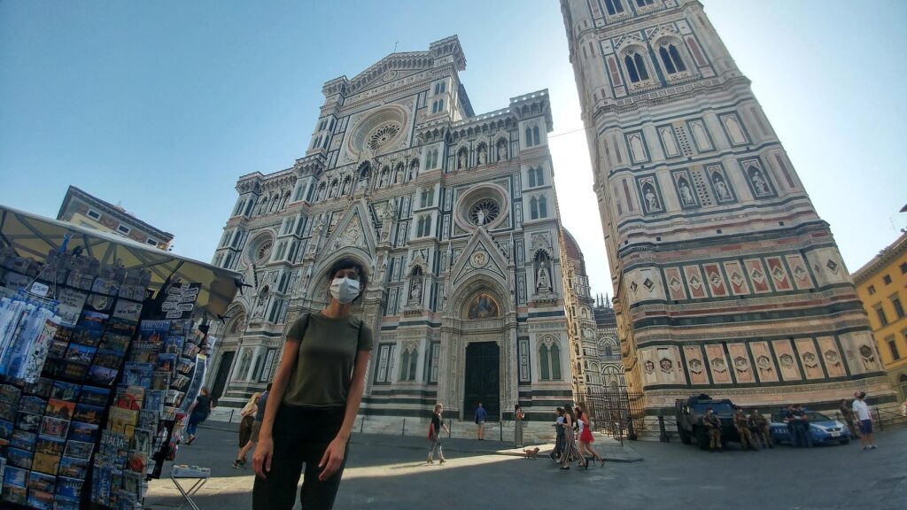 a woman in a facemask posing in front of Santa Maria Novelle Cathedral and Il Campinello in Florence Italy