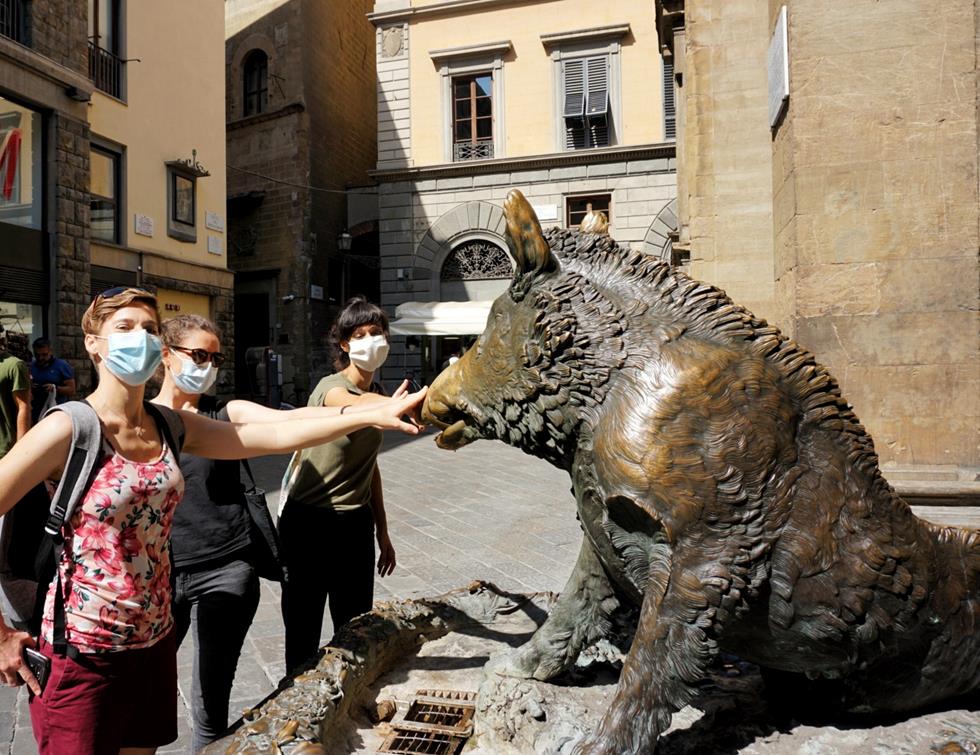 three women in face masks touching the bronze pig statue il Porcellino in Florence Italy