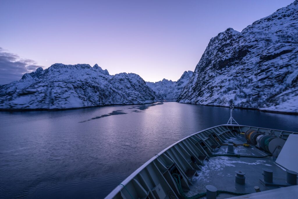 bow of ship heading toward snow covered craggy mountains in Norway