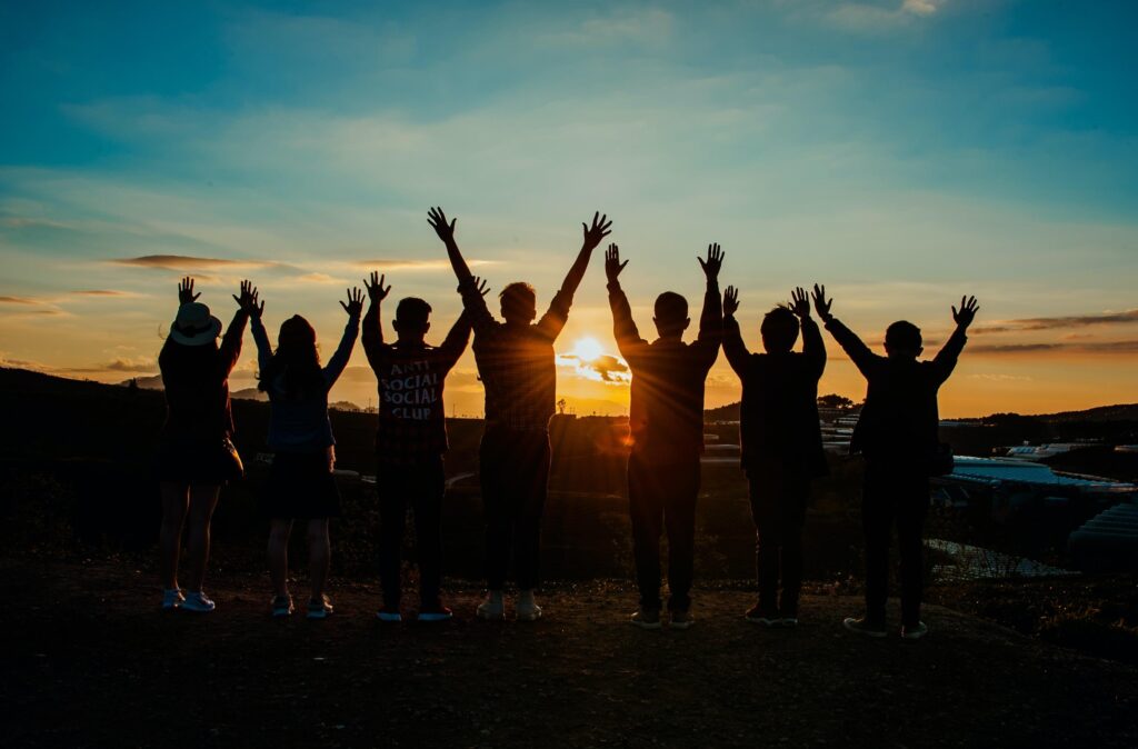 a group of people standing with their hands up facing a sunrise