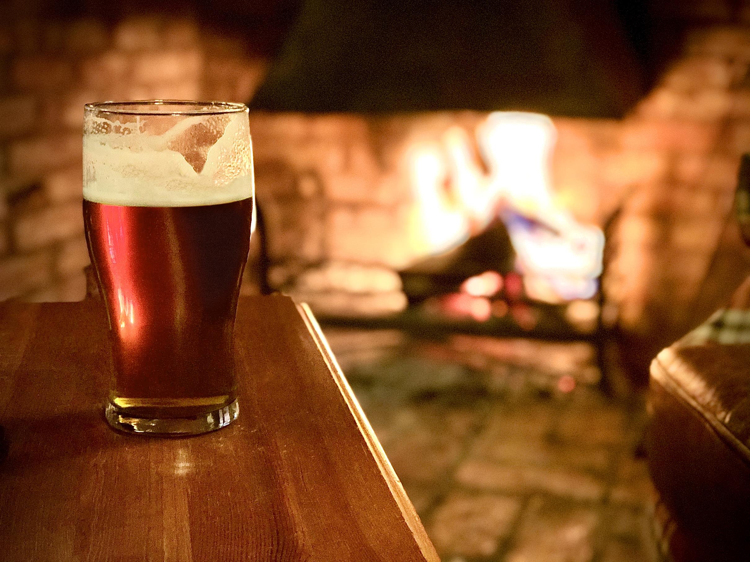 a glass of beer illuminated by the fire in the background