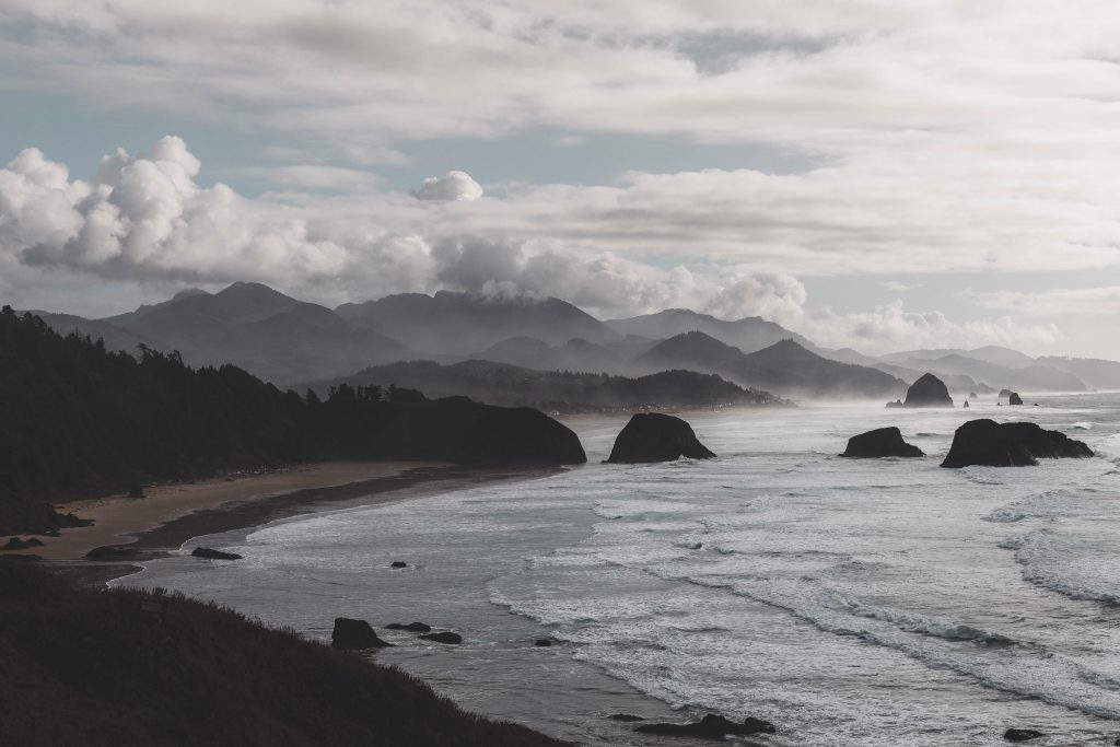 a beach and mountainous forrest in the Pacific Northewest with dramatic clouds in the sky
