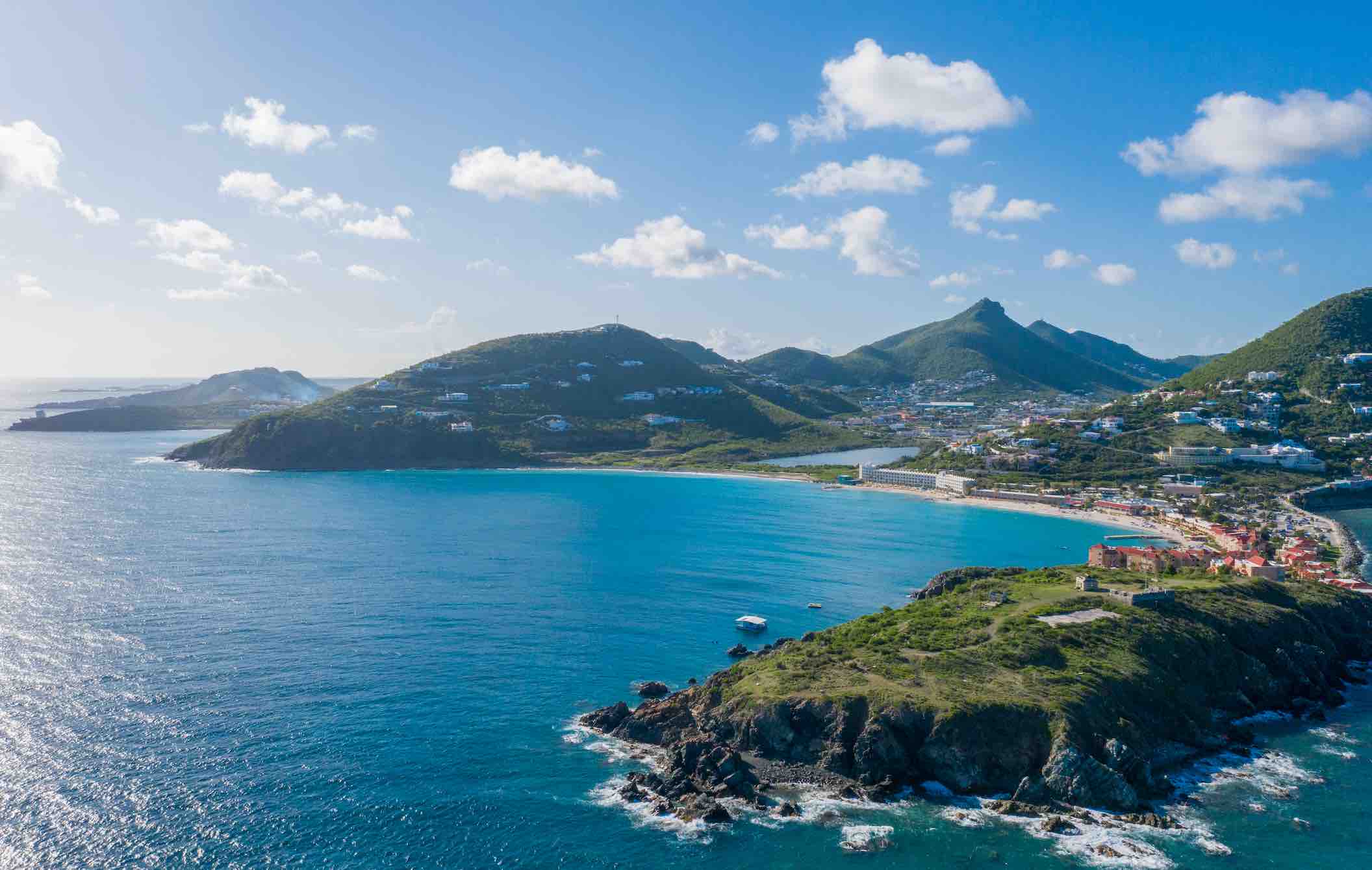 the beautiful island of St. Maarten/ St. Martin with blue sea and sky and green mountainous island dotted with houses.