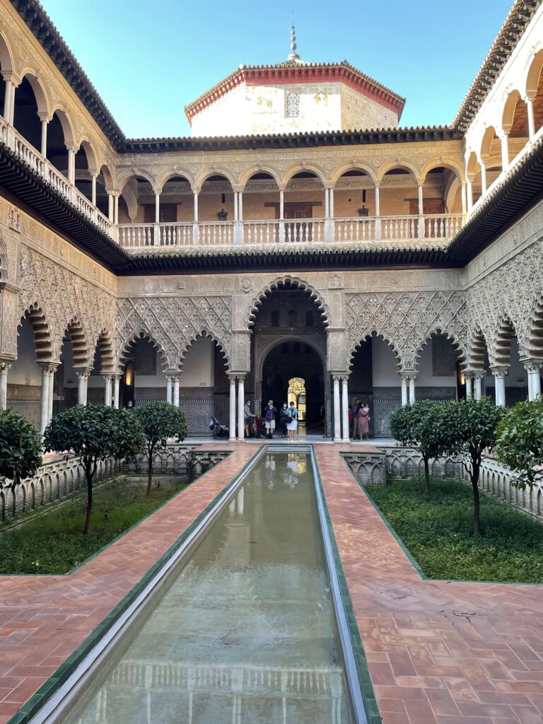 a long pool leading to impressive architecture at the Royal Alcazar Palace in Seville