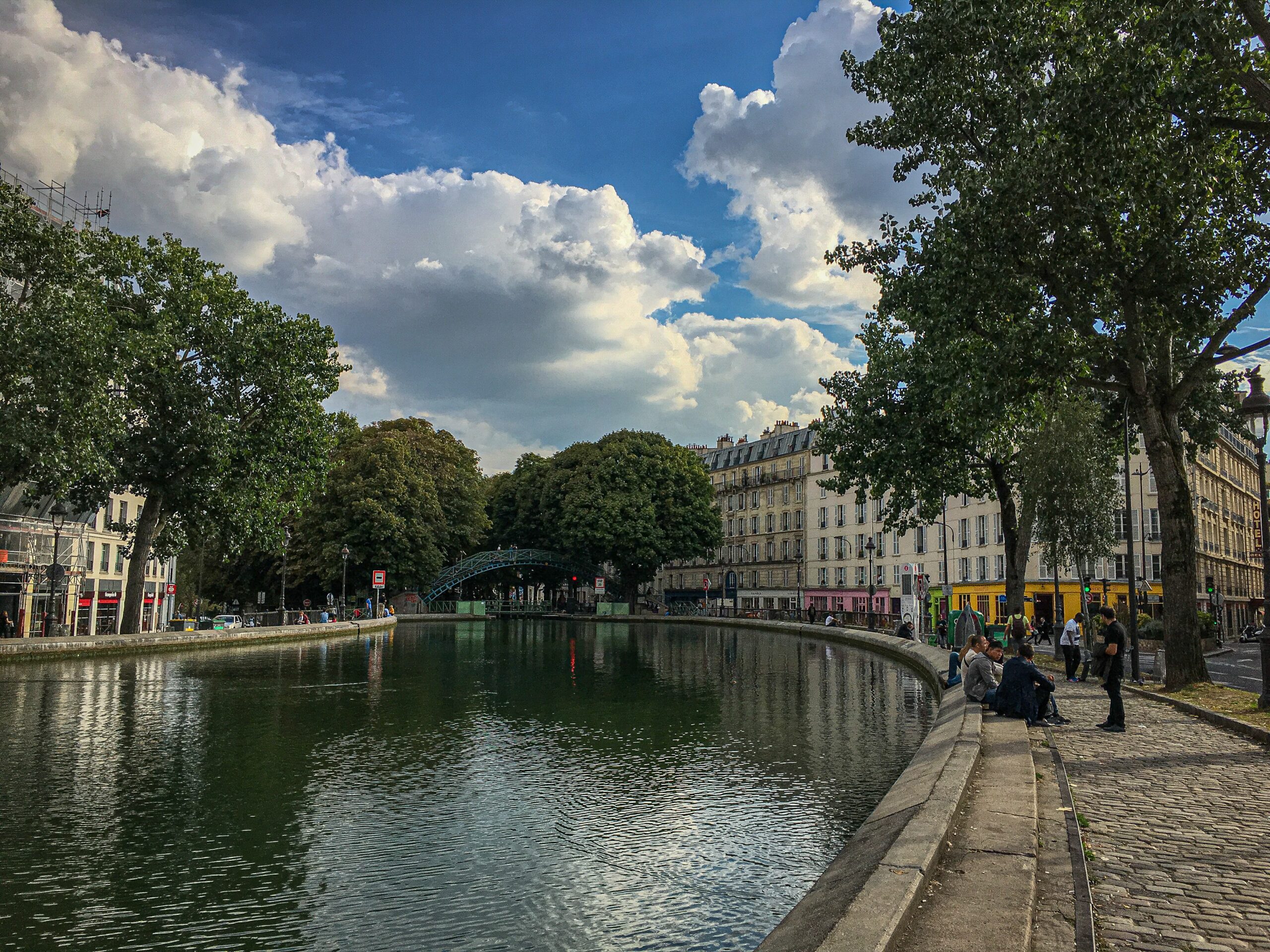 down the Canal Saint Martin in Paris with trees and people sitting along the bank