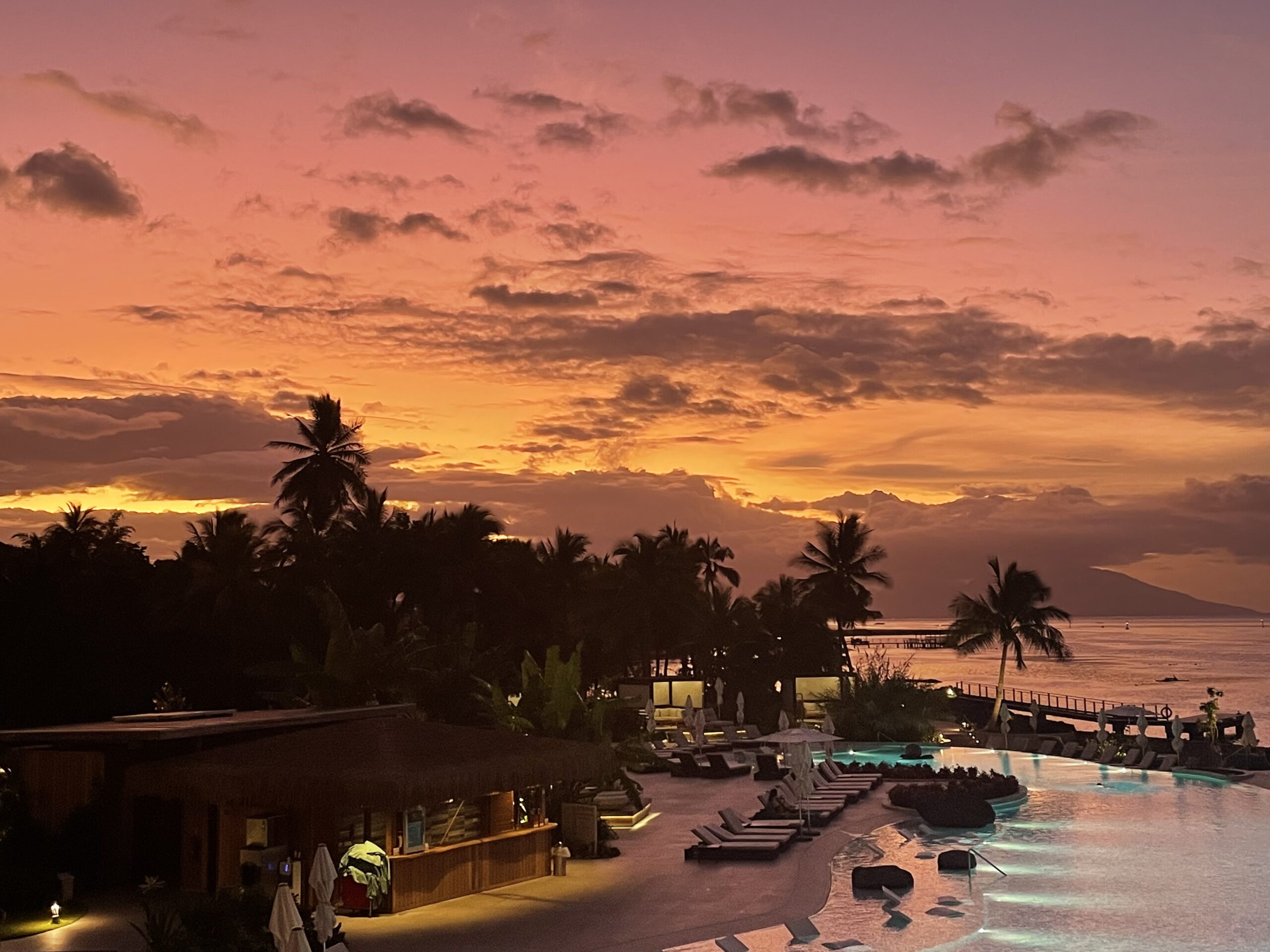 a stunning sunset over the pool and ocean at a resort in Tahiti