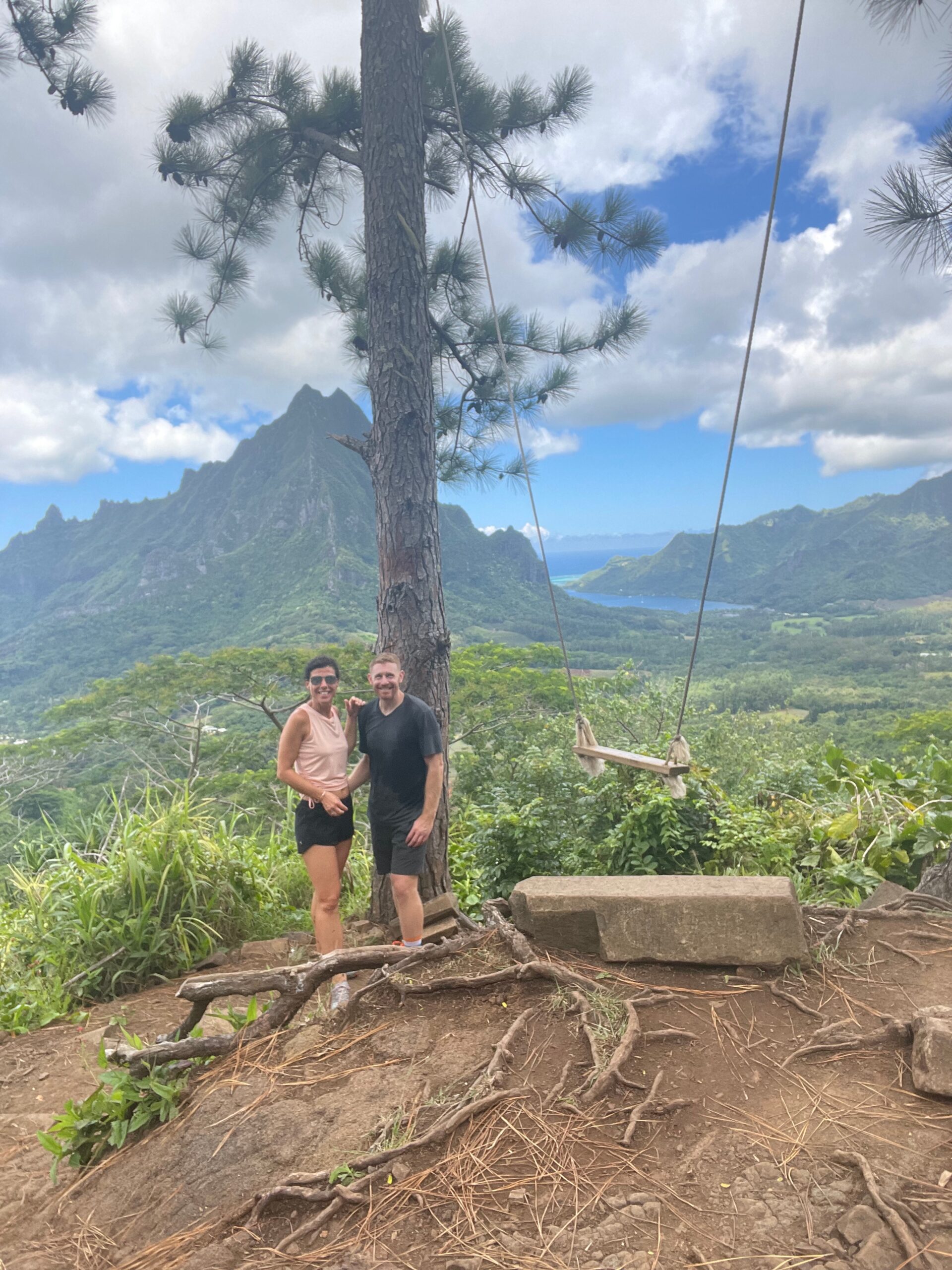 Tahiti - a honeymoon couple standing at a lookout point in Tahiti overlooking the green island with tall mountains and just a glimpse of the ocean in the background