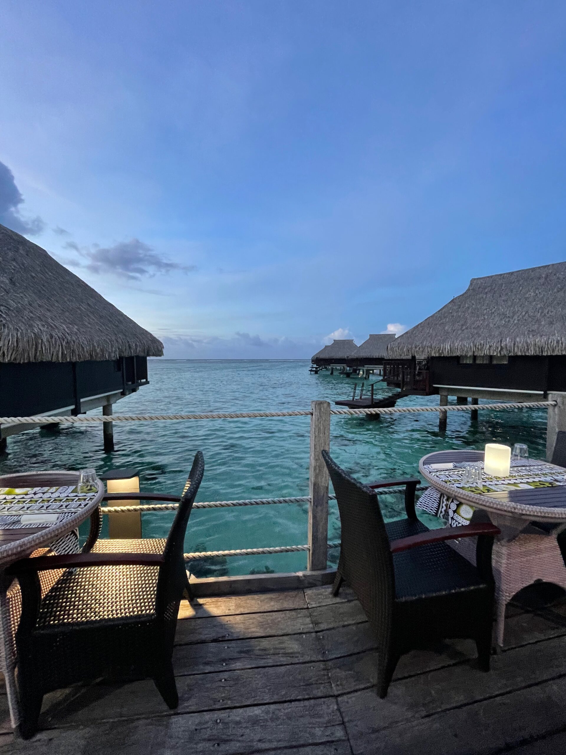 the Taha'a Pearls resort in Tahiti overwater bungalows and dining tables set up looking out over the blue water perfect for a Tahiti honeymoon