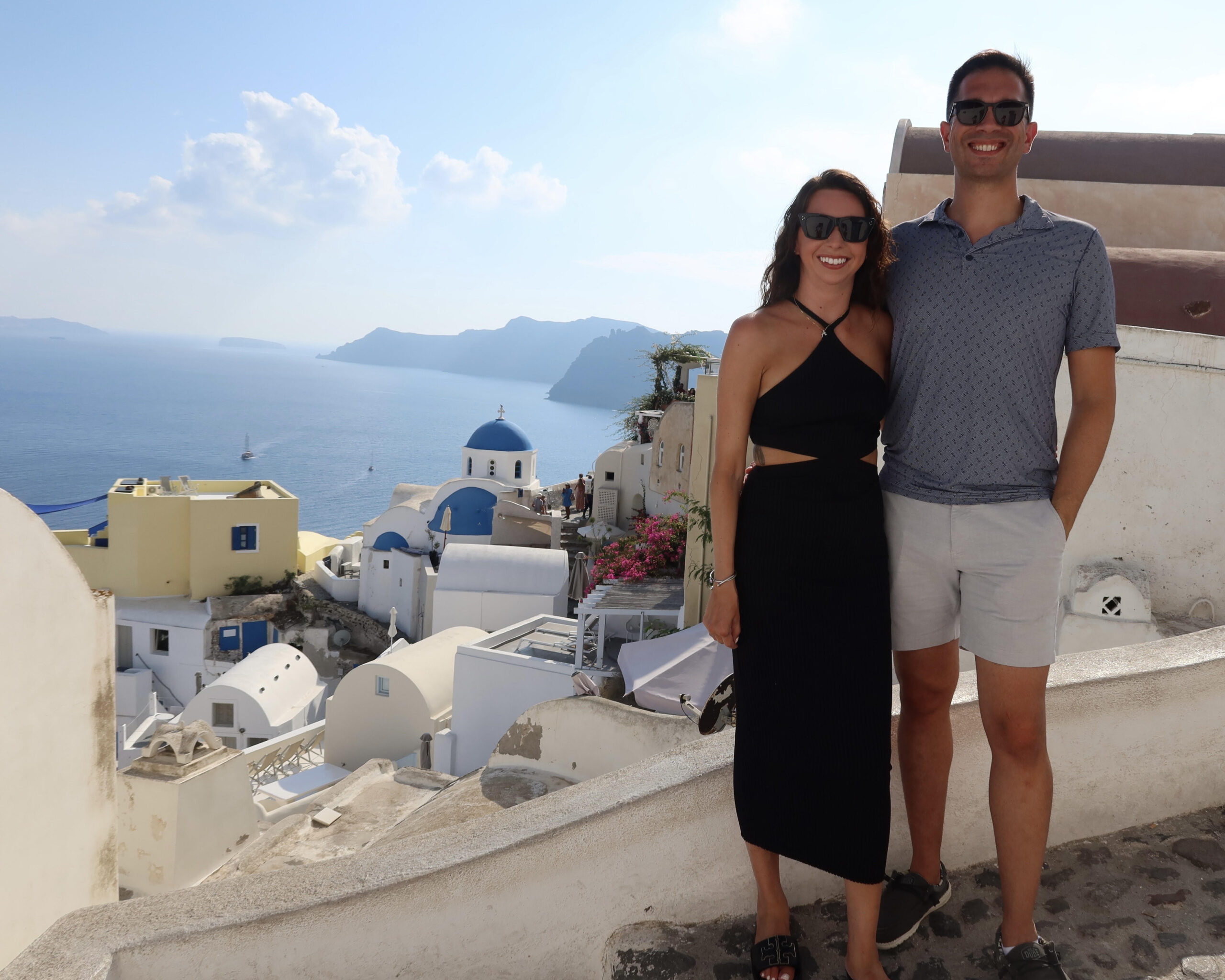 A happy couple with the white washed walls and blue domes of Santorini Greece behind them
