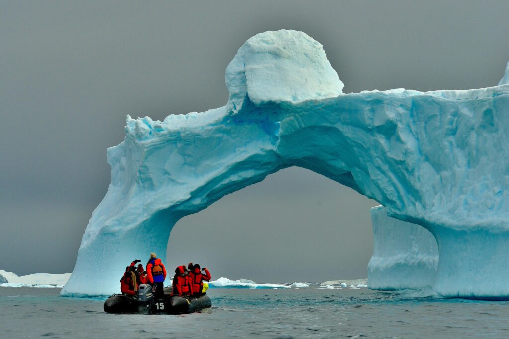a small dingy in front of an ice arch on an arctic expedition